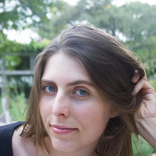 brunette girl half smiles in front of trees